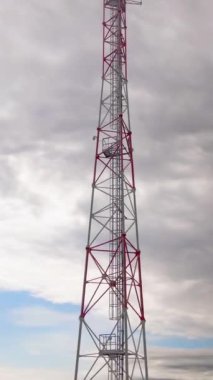 Dikey video. Mavi gökyüzü arka planında radyo iletişim anteni. Telekomünikasyon kulesi. Arkasında bulutlar olan açık gökyüzü. Uzun telefon direği ya da anten iletimi. Drone görünümü