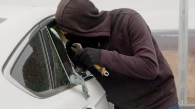 Maskeli bir adam park yerindeki lüks beyaz bir arabanın camını ağır bir aletle kırdı. Adam bir arabanın camını kırdı ve içinde bilgisayar ve diğer eşyaların olduğu bir sırt çantası çaldı. Araba hırsızı