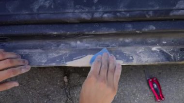 Araba parlatıcısı olan genç bir adam eski boyayı kum ve temizlemek için ince, güçlü ve sert bir siyah çarşaf kullanır. Yeni boya sıkmadan önce bir adamın ellerini araba parçalarını temizlerken yakından çek..