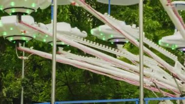 Çocuklar ve yetişkinler için yavaş dönen bir atlıkarınca. Yeşil lunaparkta ziyaretçiler için stantları olan beyaz metal atlıkarınca. Eğlence dönüşleri, turizm konsepti, tatil, aile eğlencesi, ışıklı atlıkarınca