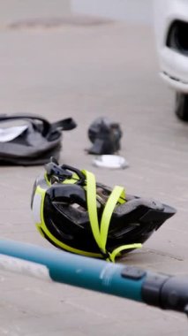 Dikey video. Trafik kazasındaki detaylar. Bir araba elektrikli scooterla birine çarptı ve koruyucu kask aşağı uçtu ve arka çanta. Arabanın parçaları asfalta düştü.