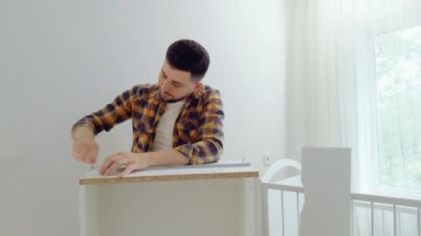 Mutlu adam çocuk odası için mobilyaları topluyor ve kameraya samimi bir şekilde gülümsüyor. Genç baba vidaları sıkıyor ve bebek karyolasını monte ediyor. Yeni doğan için mobilyaları hazırlıyorum.