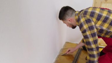 Adam süpürgelikleri doğru yere yerleştirmek için tahta zemini bıçakla temizliyor. Nitelikli kişi duvarları ölçer ve zeminin kenarlarına şeritler yerleştirmek için hazırlar..