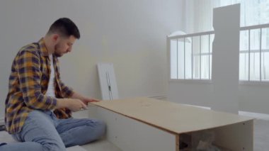Halıya oturan adam beyaz ahşap bir mobilyayı söker ve bir aletle mobilyaların vidalarını söker. Babam onu yeniden kullanmak için Childs 'ın eski beşiğinden bir fedaiyi söker.