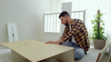 Genç adam, tornavida yardımıyla bebek için beyaz ahşap bir dolap kurmaya çalışıyor. Müstakbel baba yeni doğan bebeğin odasını hazırlıyor. Parlak bir odadan samimi bir resim.