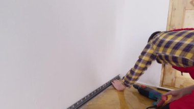 Profesyonel bir işçinin etek tahtalarını ölçüp monte etme süreci. Adam, kaideyi onarmak için duvara elektrikli matkapla delik açıyor. Evlerde ve iç mekanlarda kaliteli onarımlar