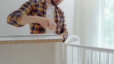 Çocuk odası için mobilyaları monte eden bir adamın yakın plan görüntüsü. Genç baba vidaları sıkıyor ve bebek karyolasını monte ediyor. Yeni doğan odası için mobilyaları hazırlıyorum.