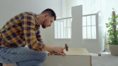 Genç baba halıya oturmuş vidaları çekiyor ve bebek beşiği için bir fedai topluyor. Çocuk odası için mobilyaları toplayan adam. Yeni doğan için mobilyaları hazırlıyorum.