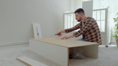 Adam beyaz ahşap bir mobilyayı söker ve bir aletle çivileri söker. Babam bebekler için bir karyola söker ve onu bir uyku yatağına çevirir. Mobilya kurulumu