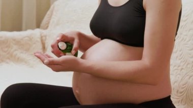 Genç hamile bir kadının, karnındaki çatlakları önlemek için avuçlarına nemlendirici yağ dökerken yakın plan görüntüsü. Hamile anne karnını sulandırıyor.