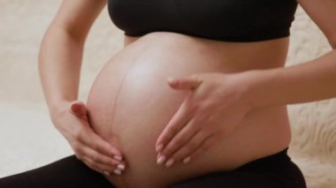 Son üç aylık dönemde hamile bir kadın göbeğine çatlakları önlemek için nemlendirici yağ sürüyor. Genç hamile bir kadının yakın plan görüntüsü karnındaki kuru deriyi nemlendirir ve masaj yapar.