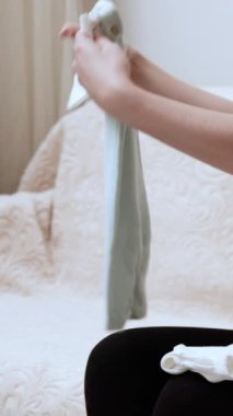 Genç hamile kadın evde yatağında oturan minik bebek kıyafetleri organize ediyor. Neşeli kadın çocuk doğurmayı bekliyor. Çocuk odası için güzel elbiseler hazırlıyor.