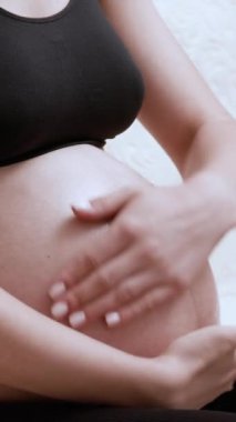 Genç hamile kadın sabahları nemlendirici krem sürerek karnına nazikçe masaj yapıyor. Üstteki kadın gerilme izlerini önlemek için cilt bakımı prosedürü uygular