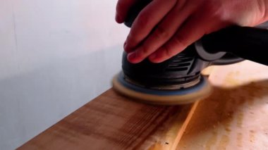 Yüzeyin kenarında öğütücü işletiyor, malzeme bile yapıyor. Genç marangoz, aletini dikkatle tutup eşitsizliği ve kıymıkları temizliyor.