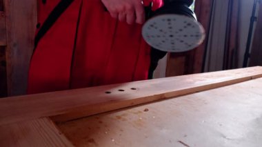 Tahta işçisi çalışma masasının üzerinde elektrikli zımpara makinesi tutuyor. Genç profesyonel, büyük yapıda çalışmadan önce makineyi çalıştırır