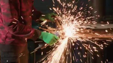 Demirci, metal yapıyı zımpara makinesiyle yüzeye değdiriyor. Profesyonel temizlik, parlak kıvılcımlara yol açan öğütücüyle pürüzlü alanları temizler