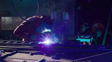 Demirci, atölyedeki kaynak makinesini kullanarak merdiveni şekillendirir. Koruyucu ekipmanlı metal işçisi, kusurları ortadan kaldırmak için metal maddenin yüzeyini parlatıyor.