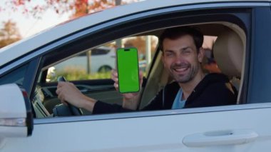 Mutlu adam otomobil paylaşımı uygulamasını pencereden telefonla gösteriyor. Gülümseyen sakallı erkek sürücü uygun bir hizmetten memnun.