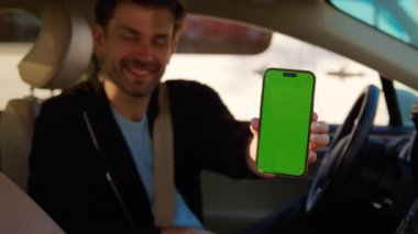 Şoför koltuğundaki mutlu adam araba paylaşım uygulamalı akıllı telefonu gösteriyor. Adam şehirde araç kiralama hizmetinden memnun olduğunu ifade ediyor.