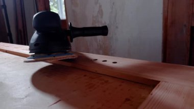 Elektrikli zımpara makinesi geniş atölyedeki ahşap yüzeyde yatıyor. Sapı kontrol ve zımparalama diski yüzey ile teması sürdürmeye yardımcı olur