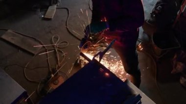 İşçi, metal yapıyı klempte tutuyor. Üniformalı demirci, düzgün olmayan parçaları söküp atölyede pürüzsüz hale getirmeye çalışır.