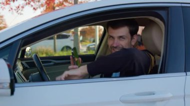 Adam sunulan emirle akıllı telefon ekranını göstererek otomobil penceresinden sarkıyor. Gülümseyen genç sürücü çevrimiçi kullanışlı hizmetten memnun olduğunu ifade ediyor