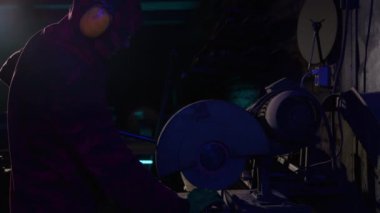 Demirci makinenin kapağını gıcırdatmak için tekerlekle kapatıyor. Adam profesyonel olarak metali işliyor ve yarı karanlık bir görünüme sokuyor.