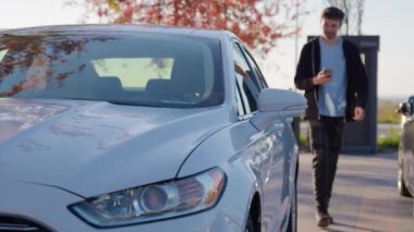 Adam kapıyı açmak için elinde telefonla araba paylaşan bir araca doğru yürüyor. Erkek sürücü akıllı telefondan yüklenmiş çevrimiçi uygulama kullanarak araba açar