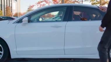 Adam elinde akıllı telefonla araba paylaşan bir araca biniyor. Erkek sürücü, telefona yüklenmiş mobil uygulamayla kiralık arabayı sanal anahtarla açar