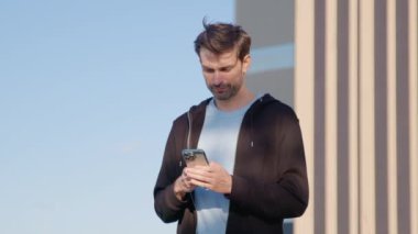 Ellerinde telefon olan adam etrafa bakıp araba paylaşım aracı arıyor. Erkek, mobil uygulama üzerinden kayıtlı aracın yerini bulmaya çalışıyor