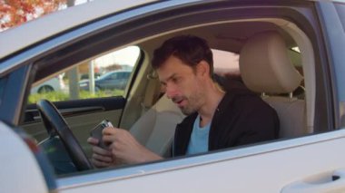 Gülümseyen adam telefonda araba paylaşım aracında oturuyor. Erkek, araba kiralama onayı beklerken mobil uygulamasında araba kullanma simülasyonu yapıyor