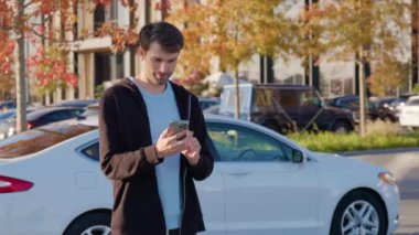 Akıllı telefonu olan mutlu bir adam araba paylaşım uygulaması aracılığıyla araba kiraladı. Erkek blogcu, araba kiralama detaylarını cep telefonundan kontrol ediyor.