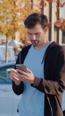 Gülümseyen adam kısa bir yolculuktan sonra araba paylaşım servisini öder. Mutlu müşteri işlem dikey çekimini tamamlamak için telefon uygulamasını kullanır