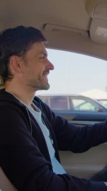 Gülümseyen adam otoparktaki araba kuaförüne bakıyor. Mutlu adam direksiyonu tutuyor ve otomatik gösterge paneline dikey bakıyor.