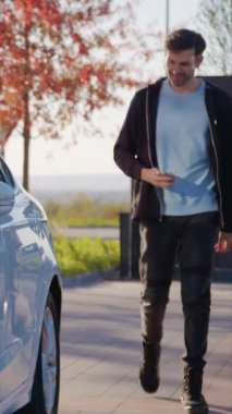 Adam otoparktan sipariş edilen araç paylaşımını alıyor. Sürücü kapıyı telefonla açıyor ve direksiyonun arkasına dikey çekimle geçiyor.