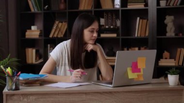 Kadın öğrenci, kütüphanedeki masada oturan dizüstü bilgisayardan akademik içeriği inceliyor. Uzun saçlı genç bayan eğitici görüşleri not etmek için kalem tutuyor.