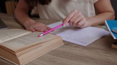 Odaklanmış kız öğrenci, detaylar için kitaba güvenen pembe kalemle defterde ana hatları oluşturur. Mezuniyet sınavı kütüphanede yapılır