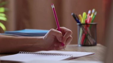 Kadın öğrenci sol elini not defterine temel akademik taslakları yazıyor. Kadın, okuma odasında oturan kalemle eğitici sezgileri kaydediyor.