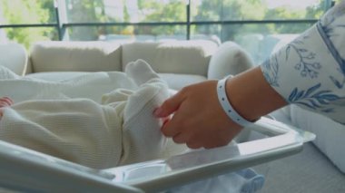 Modern bir özel doğum hastanesinde beşiğinde yeni doğmuş bir bebek. Küçük, neşeli ve enerjik bir bebeğin portresi ve elinde bebek kimlik etiketi olan bir annenin elleri. Sağlık, hamilelik ve annelik kavramı