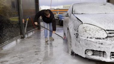 Arabayı en ufak detayına kadar temizlemek için elle yıkama. Adam arabayı toz ve kiri temizlemek için özel bir deterjanla yıkıyor. Oto yıkamada sabunlu suyla dolu siyah bir araba.
