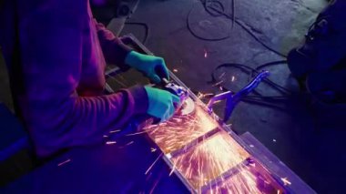 Usta demirci atölyesinde demirden bir şey yapıyor. Eldivenli bir adam öğütücüyle bir demir parçasını düzleştirir. Metal ürünleri üreticisi. Kıvılcım