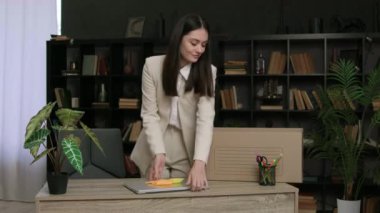 Neşeli ifadesi olan genç bir kadın modern dizüstü bilgisayar taşıyor. Gülümseyen iş kadını, cihaz ve ofis malzemelerini karton kutuya yerleştirir.