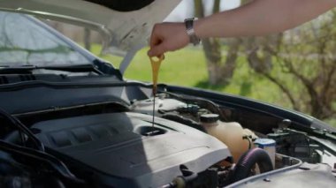 Çubuklu adam motor yağı seviyesini kontrol ediyor. Özel bir alet tutan adam, sıvıyı analiz etmek için uzun metal çubuğu halkayla dibe indiriyor.