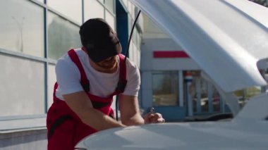 Tamirci araba servisindeki aracı tamir etmek için ingiliz anahtarı kullanıyor. Ciddi adam büyük binanın yakınındaki otomobil arızasını düzeltmek için otomatik kaput altında çalışıyor