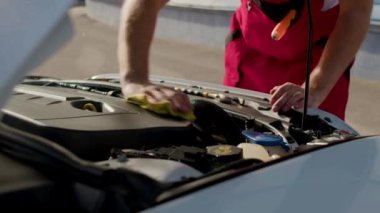 Araba servisi teknisyeni, araç motorunu paçavrayla siliyor. Üniforma giyen erkek uzmanlar araba lekelerini onarmayı ve incelemeyi bitiriyor.
