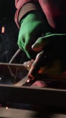 Deneyimli demirci, karanlık atölyede parlak kıvılcımlar saçan metal kaynak yapar. Kaynakçı geleneksel metal işçiliği sanatını gösteriyor