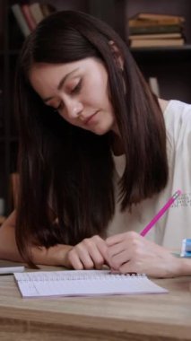 Bayan öğrenci kütüphanede masasında otururken çevrimiçi sunumun özetini not alıyor. Solak kadın akademik materyalleri dizüstü bilgisayardan not defterine kopyalıyor.