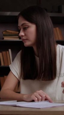 Genç bir kız öğrenci dizüstü bilgisayarla çevrimiçi konferans dinlerken özet yazar. Kadın mezun, okuma odasında ders çalışarak vakit geçirir.