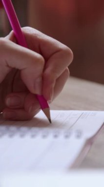 Kadın öğrenci, tahta masada oturan kalemle sol eliyle deftere yazar. Bayan, not defterine anahtar noktaları yazmak için üniversite sınavına hazırlanıyor.