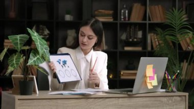 Klasik takım elbiseli bir kadın bilgisayarda önemli bir tartışma yapıyor ve müşterilerine olası iş geliştirme ülkeleri hakkında tablolar, istatistikler ve tartışmalar gösteriyor. Ofis işi